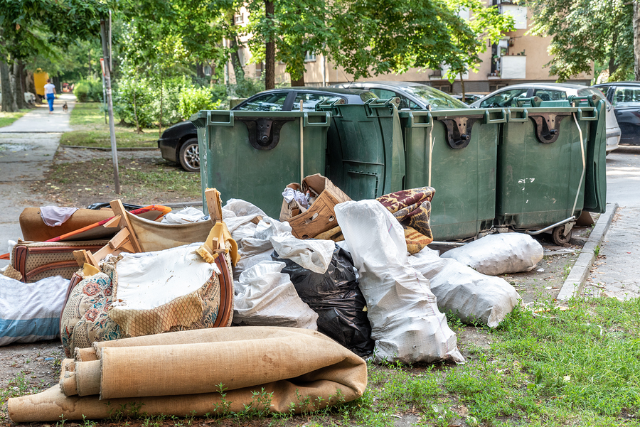 Home furniture thrown in the garbage on the street in the city near plastic dumpster cans littering and polluting the town and environment as junk and trash